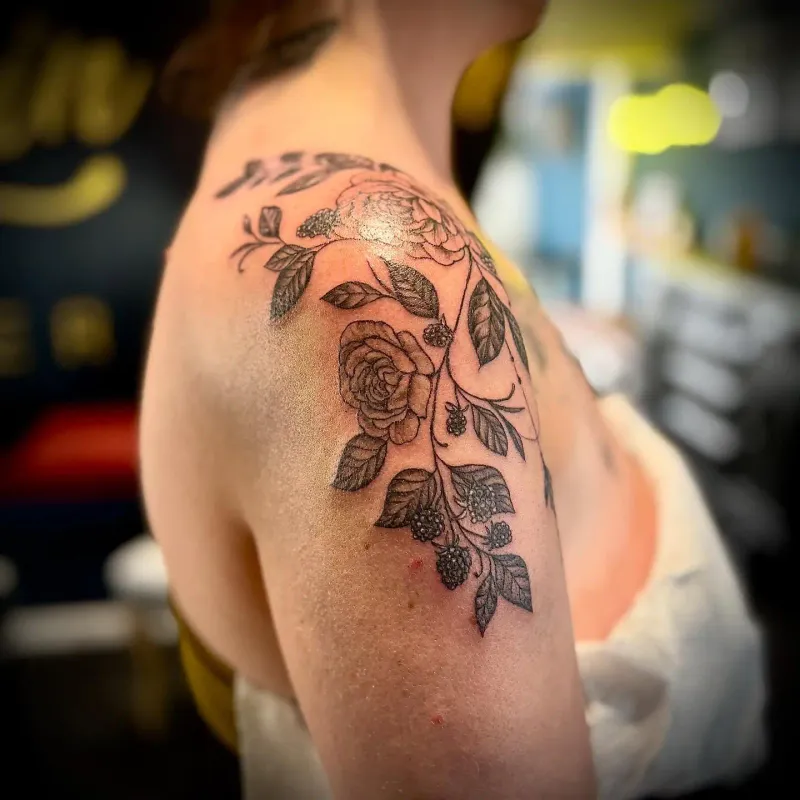 Side profile of botanical shoulder tattoo with berries and leaves